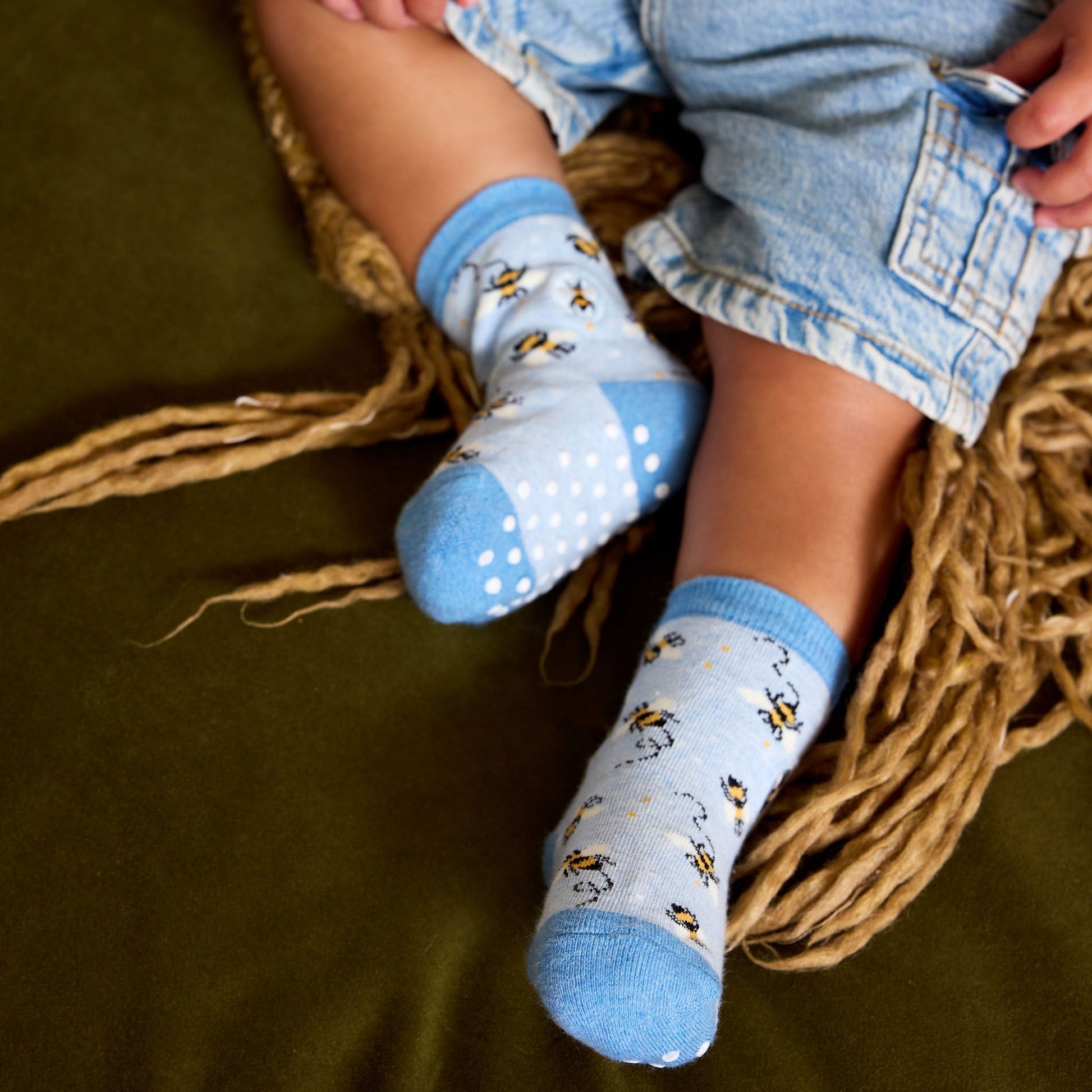 Child's legs wearing blue socks with bee pattern on a woven basket