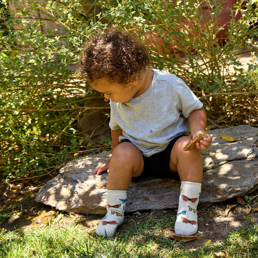 Child sitting on a rock outdoors, wearing socks with butterfly designs.