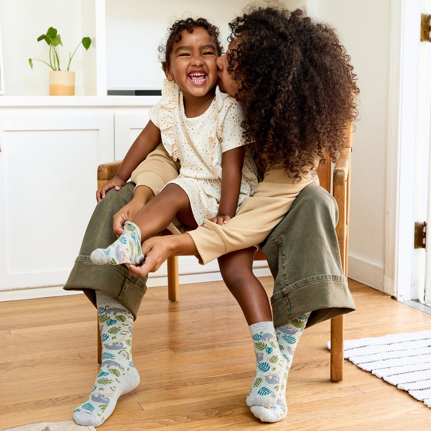 Two children sitting on a chair, one whispering to the other, wearing patterned socks.