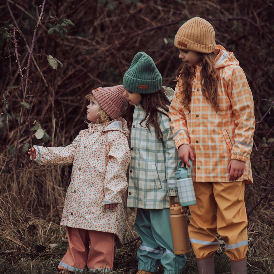 Three children in colorful raincoats and hats standing in a natural setting.