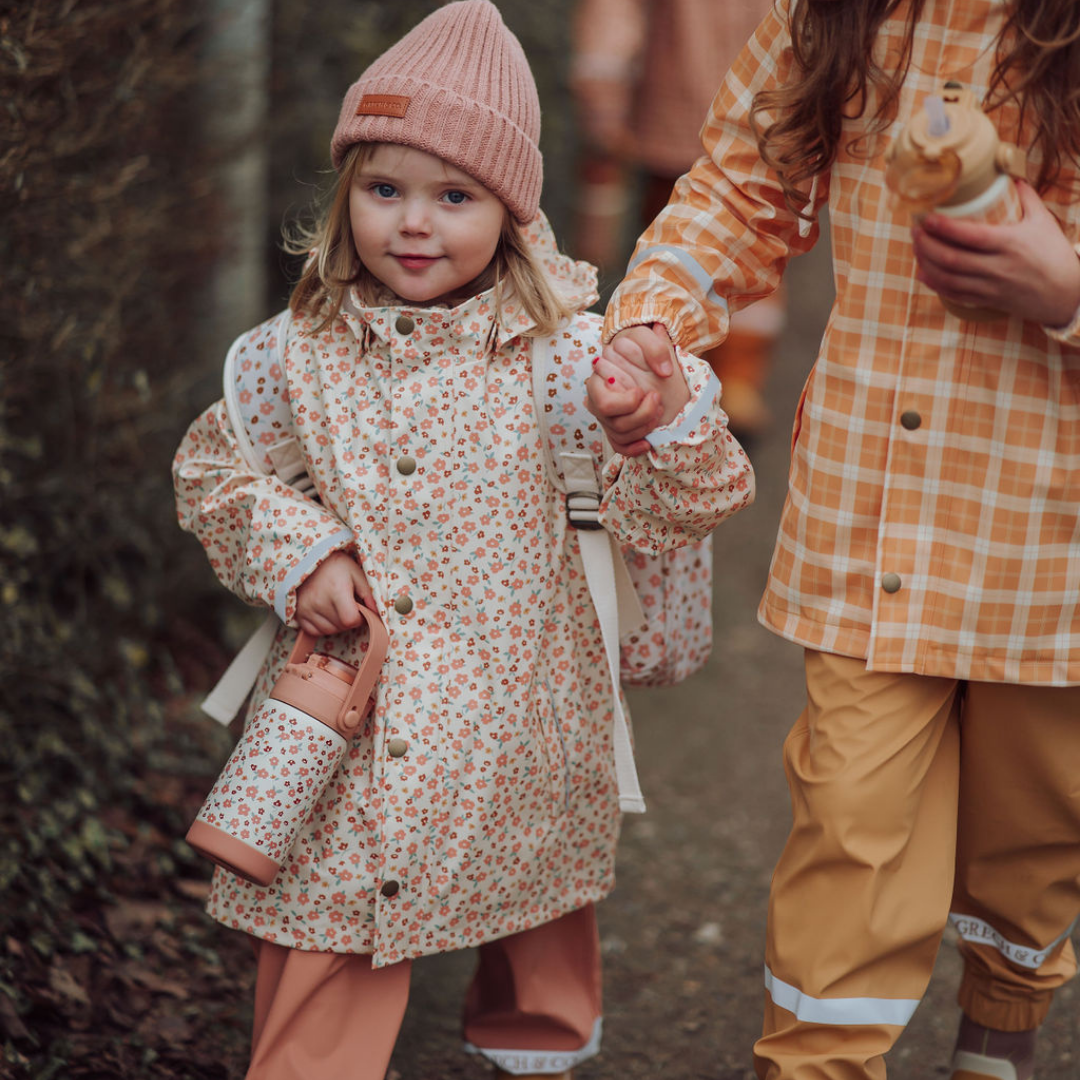 Two children in raincoats and hats holding hands outdoors.