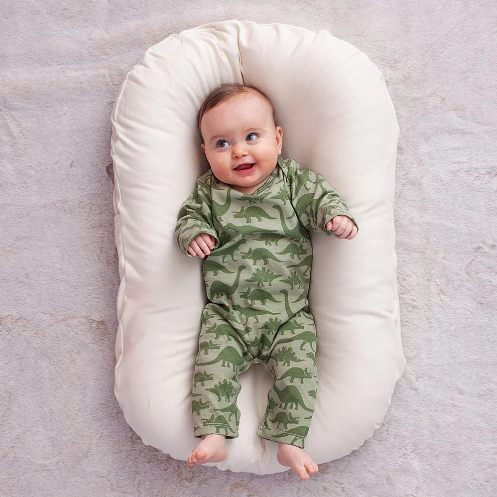 Baby in a dinosaur-patterned romper lying on a white cushion