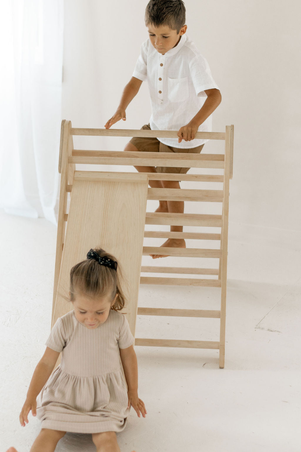 Two children playing with a wooden climbing toy on a white background