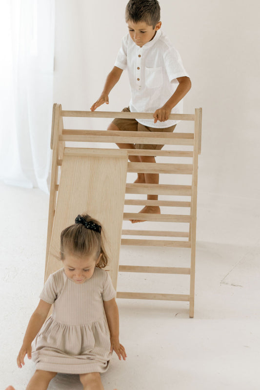 Two children playing with a wooden climbing toy on a white background