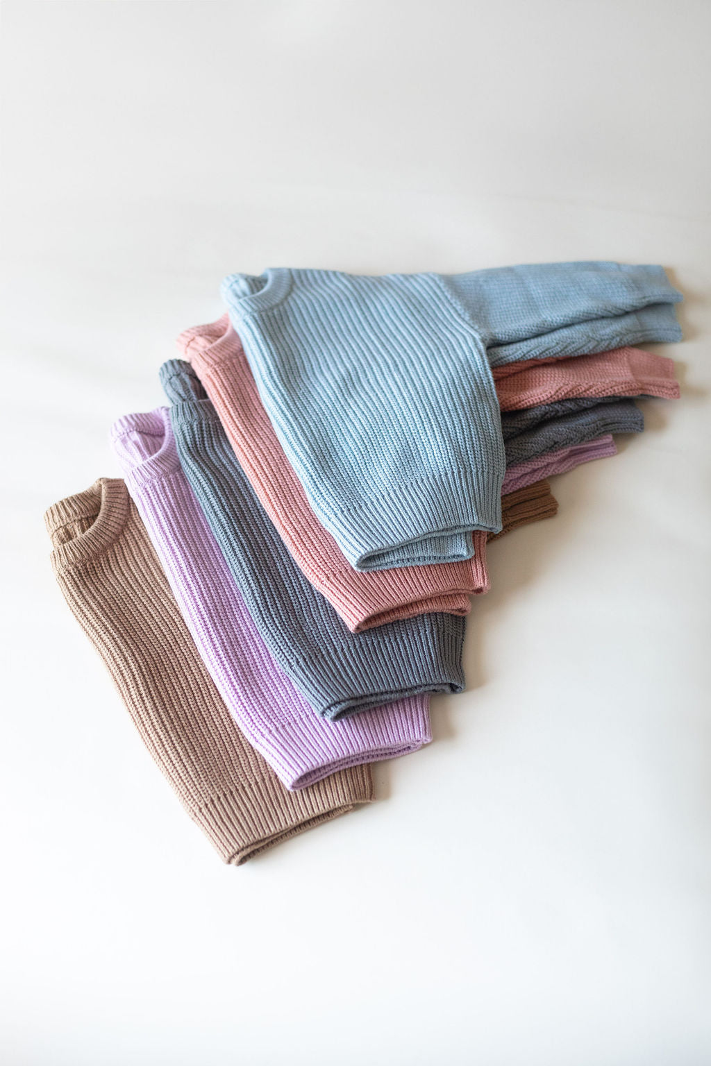 Stack of folded ribbed knit garments in various pastel colors on a white background