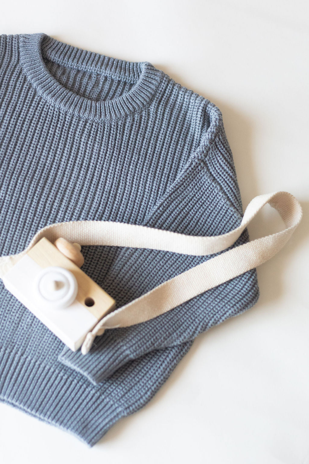 Blue ribbed sweater with a white camera and strap on a light background
