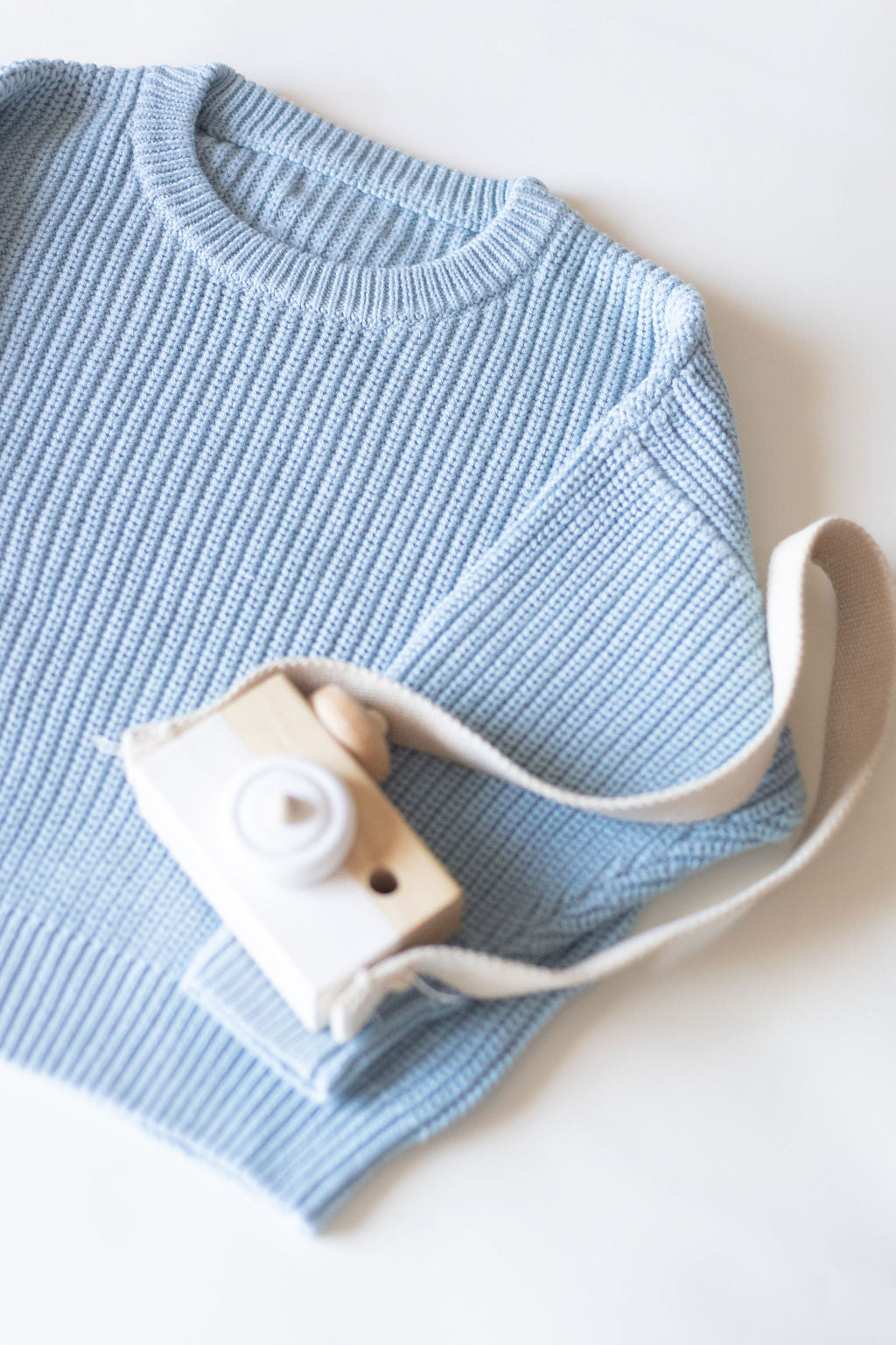 Light blue sweater with a white camera and strap on a white background