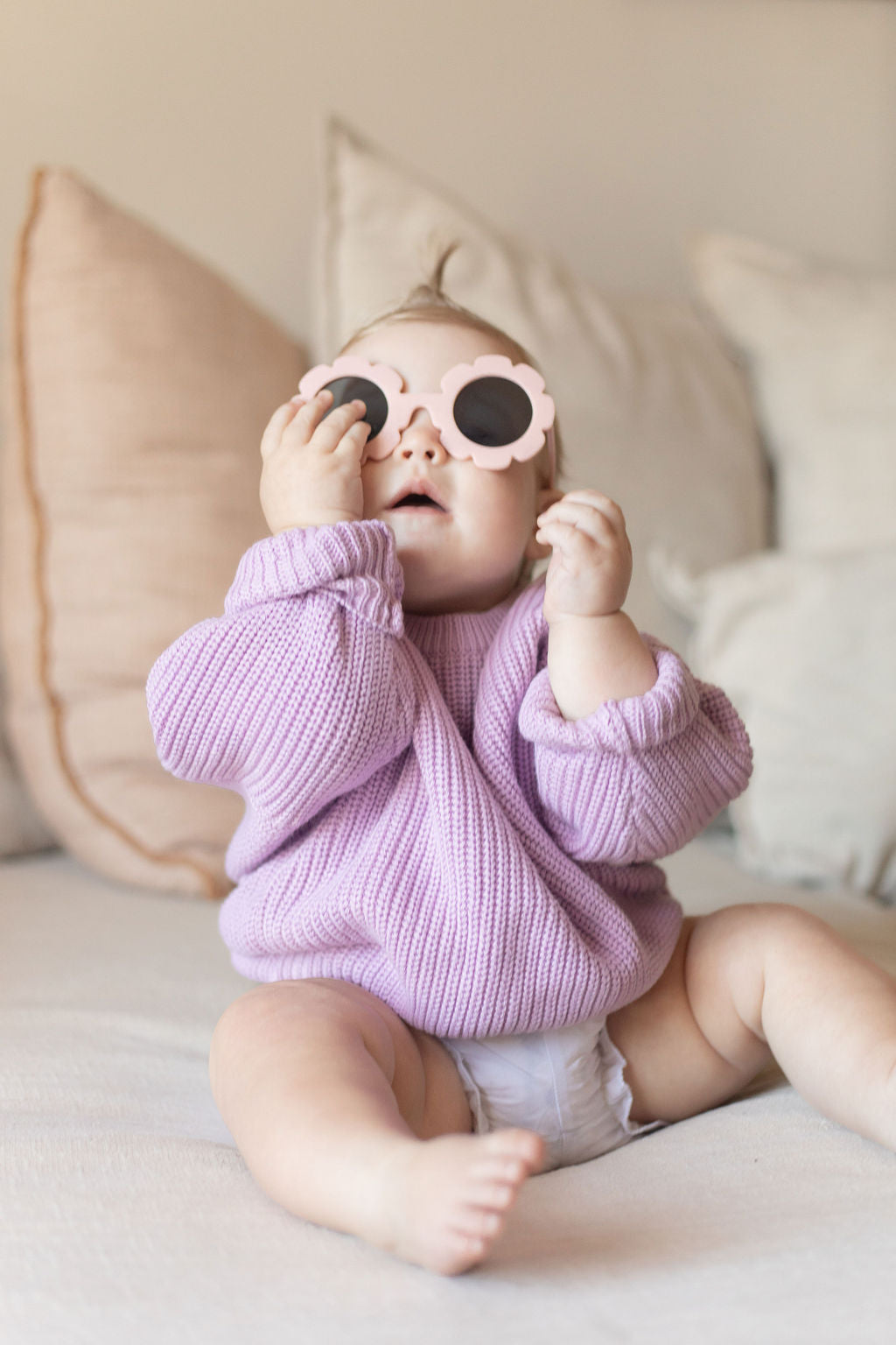 Baby wearing a pink sweater and sunglasses sitting on a couch.