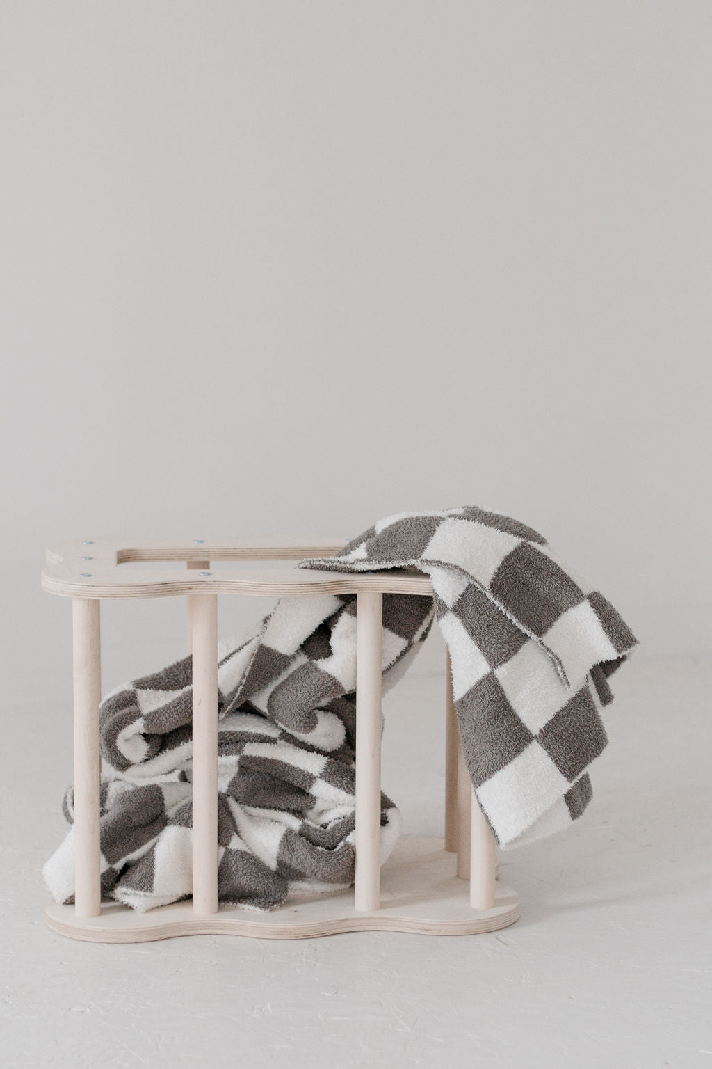 Checkered blanket draped over a wooden basket on a light gray background