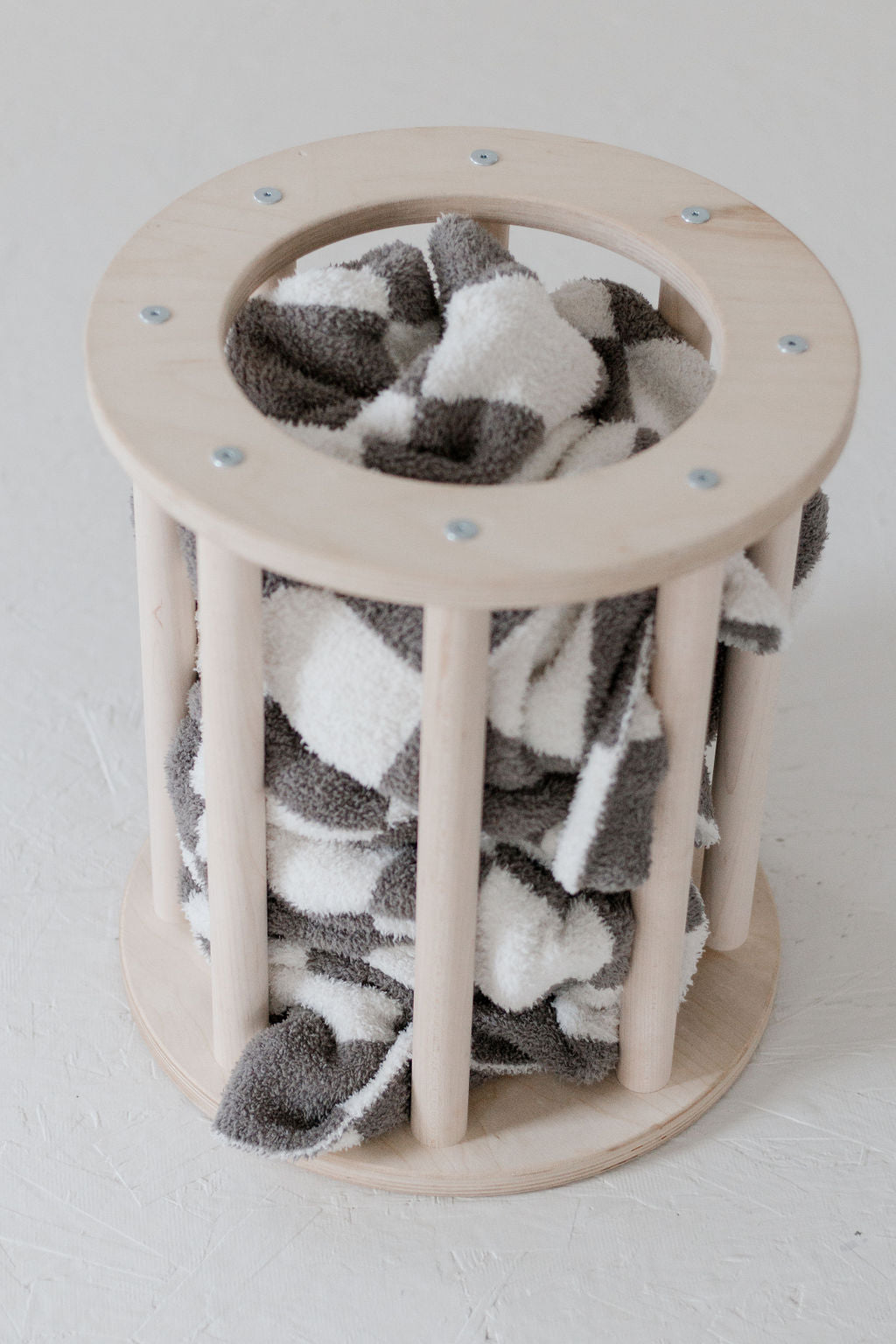 Cat toy with a cylindrical wooden frame and gray and white fabric inside on a light background