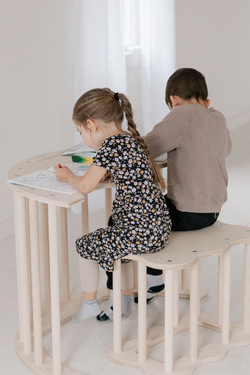 Two children sitting at a small wooden table in a bright room.