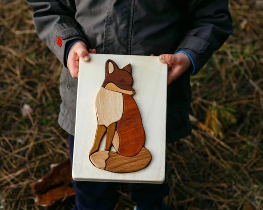 Person holding a wooden fox puzzle in an outdoor setting