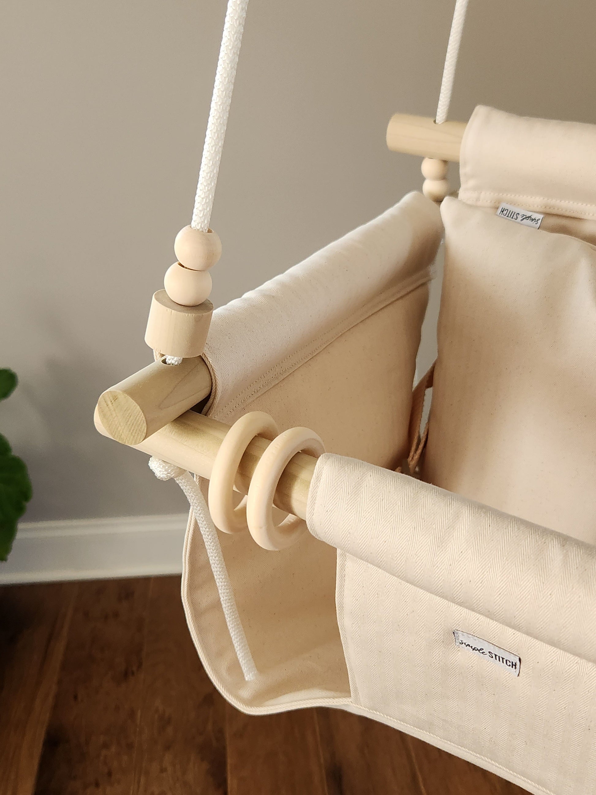 Beige baby swing with wooden poles on a neutral background