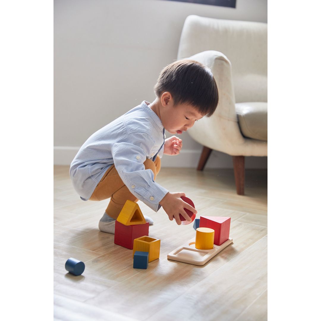Child playing with colorful building blocks on a wooden floor.
