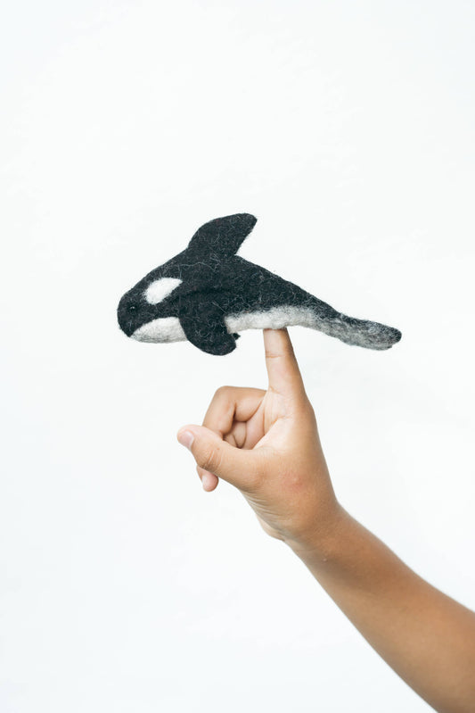Hand holding a felt whale finger puppet against a white background