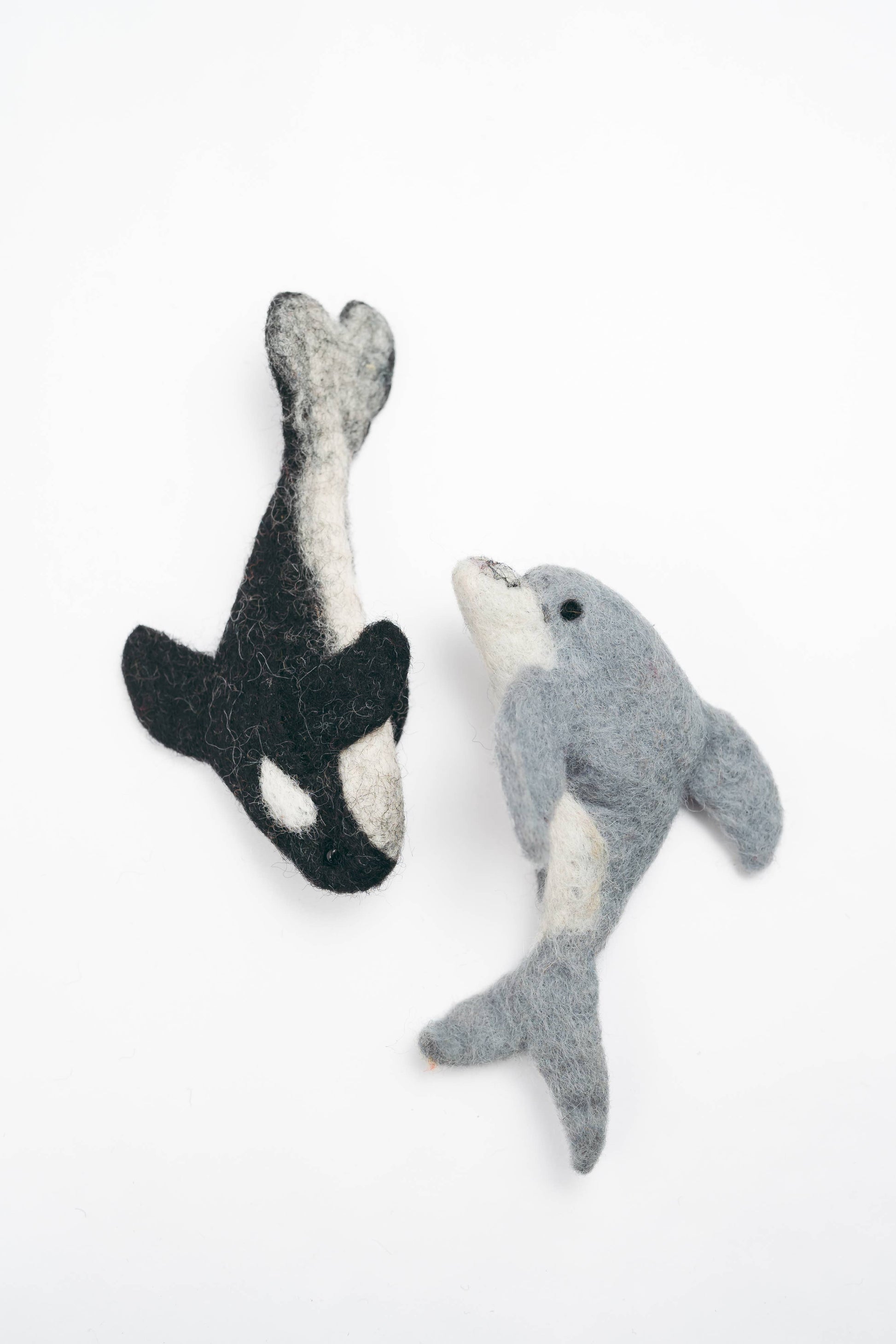 Two felted whale toys, one black and white and one gray, on a white background