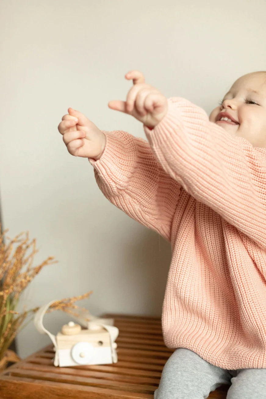 Child wearing a pink sweater with a neutral background