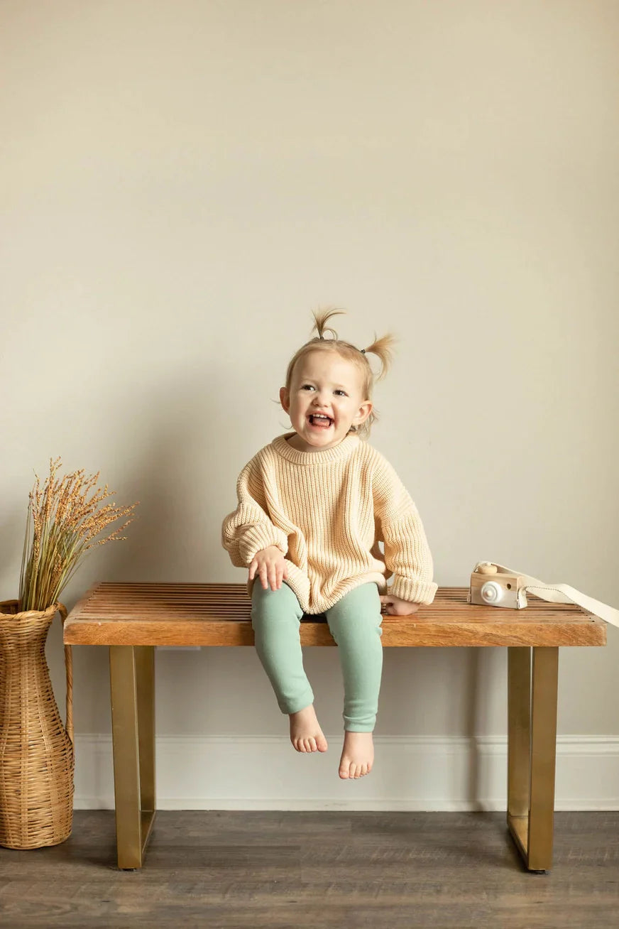 Child sitting on a wooden bench with a neutral background