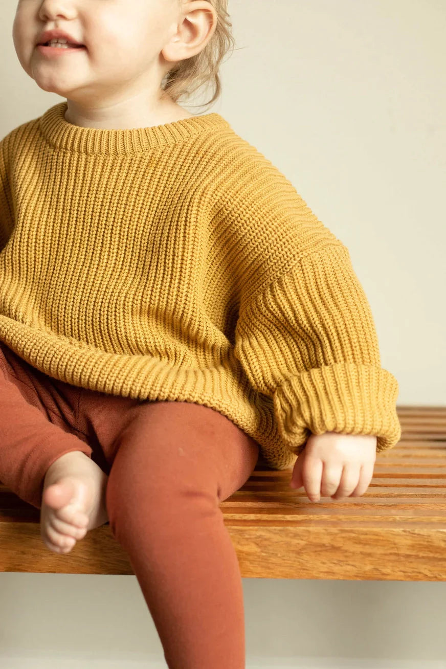 Child wearing a mustard yellow knitted sweater sitting on a wooden surface.