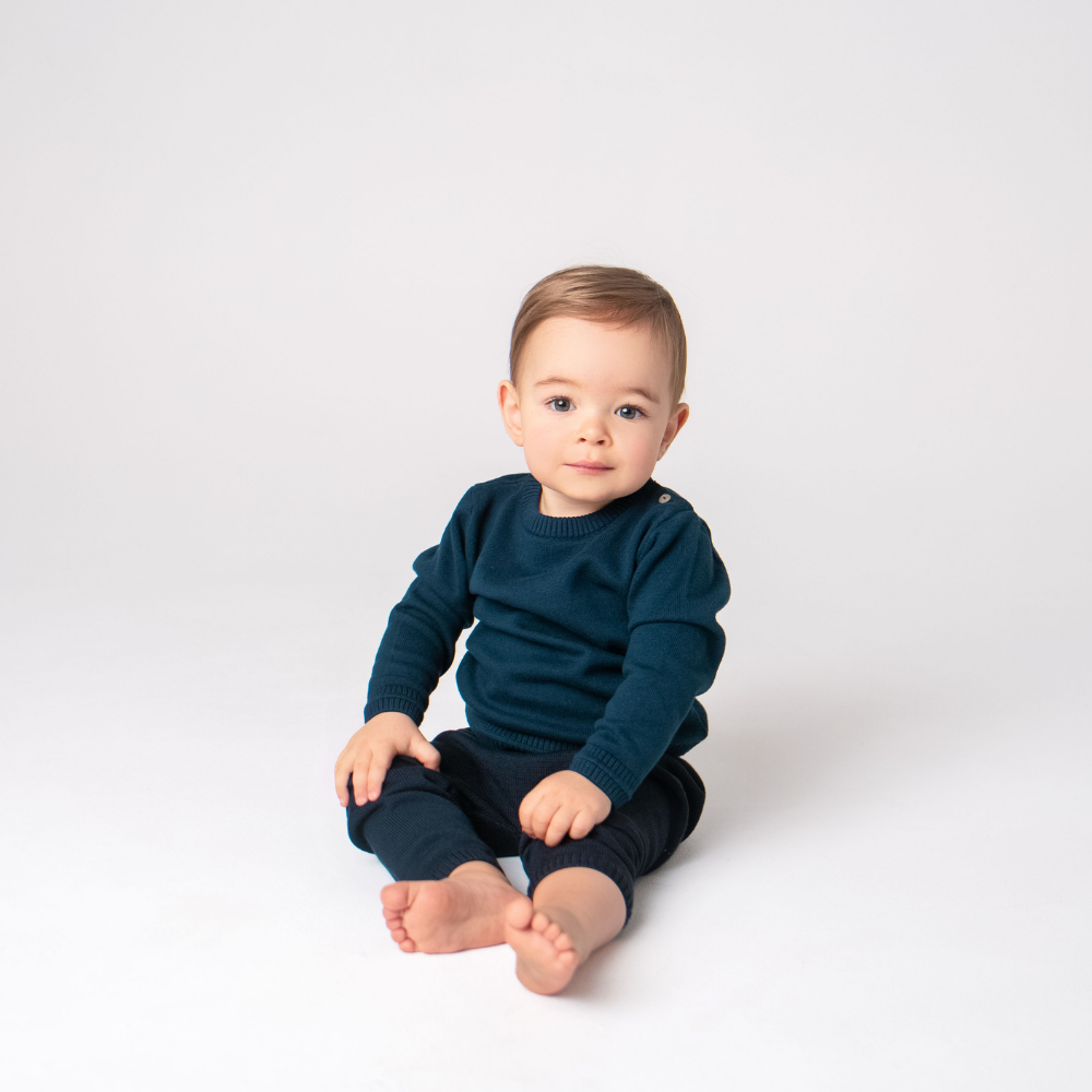 Baby wearing a dark blue sweater and pants sitting on a white background