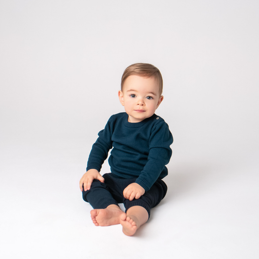 Baby wearing a dark blue sweater and pants sitting on a white background