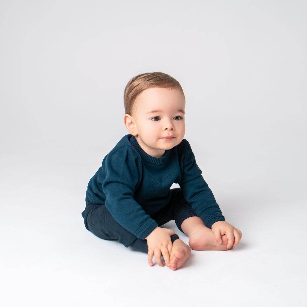 Baby wearing a dark blue outfit sitting on a white background