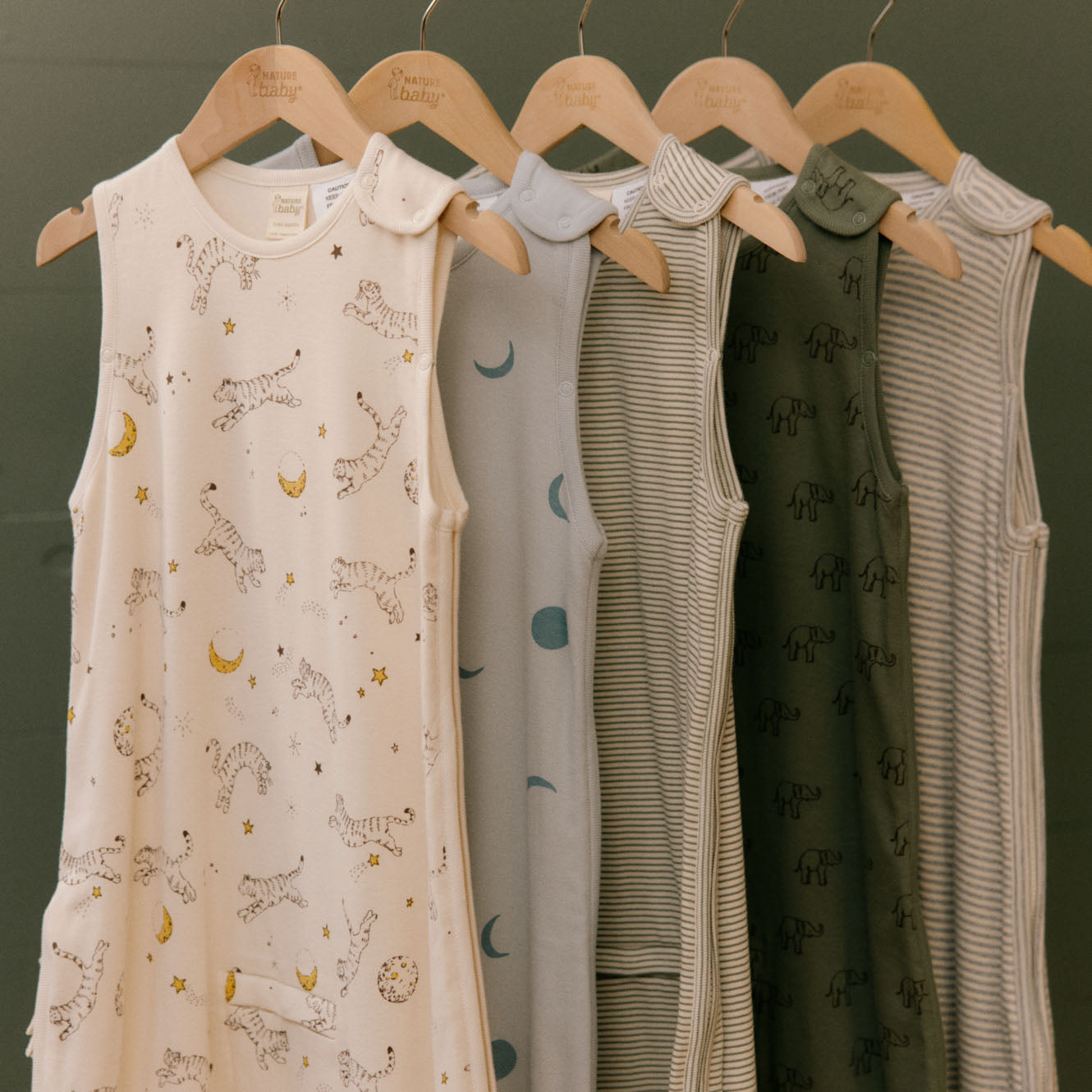 Children's sleeveless dresses with various patterns on hangers against a green background