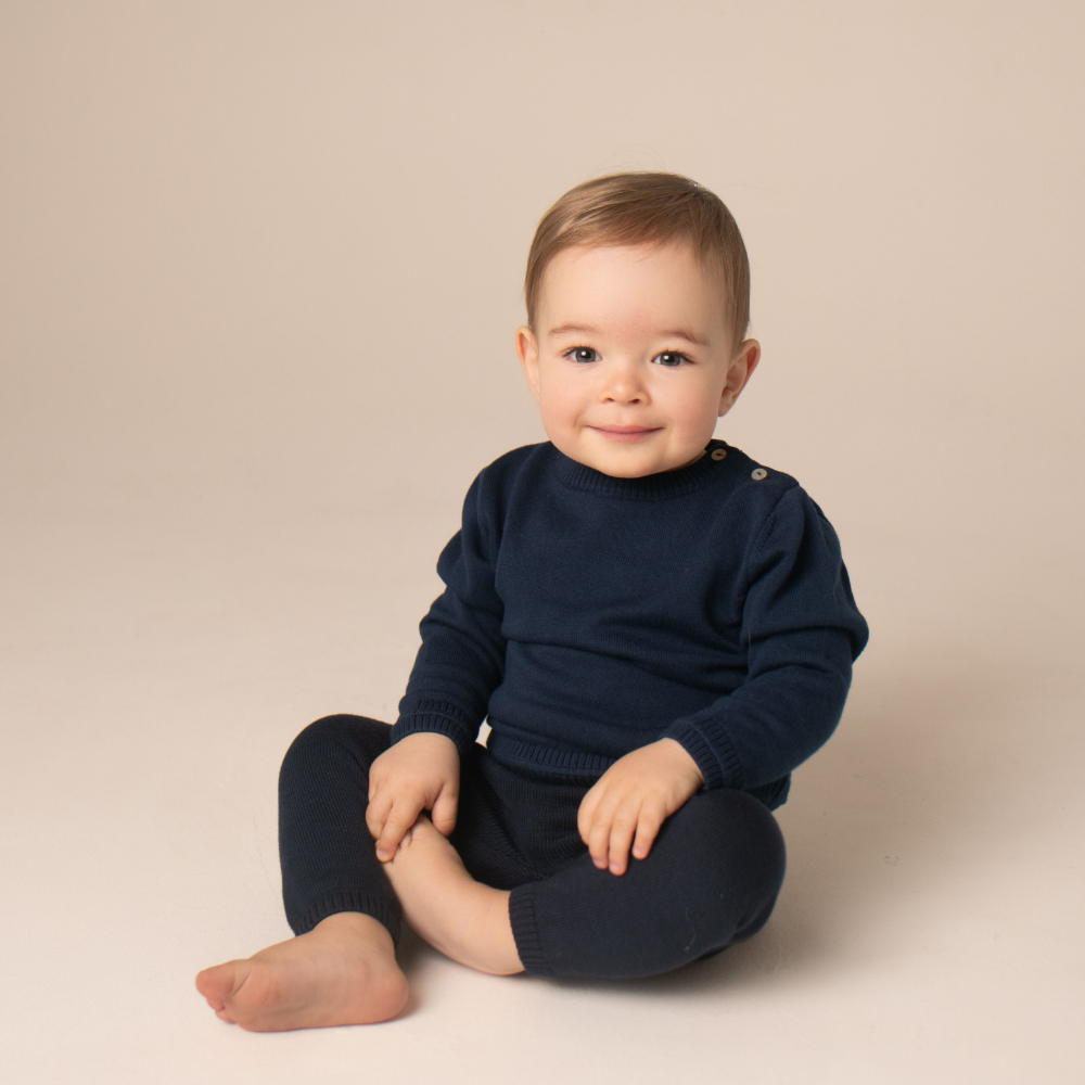 Child wearing a navy blue sweater and pants sitting on a beige background