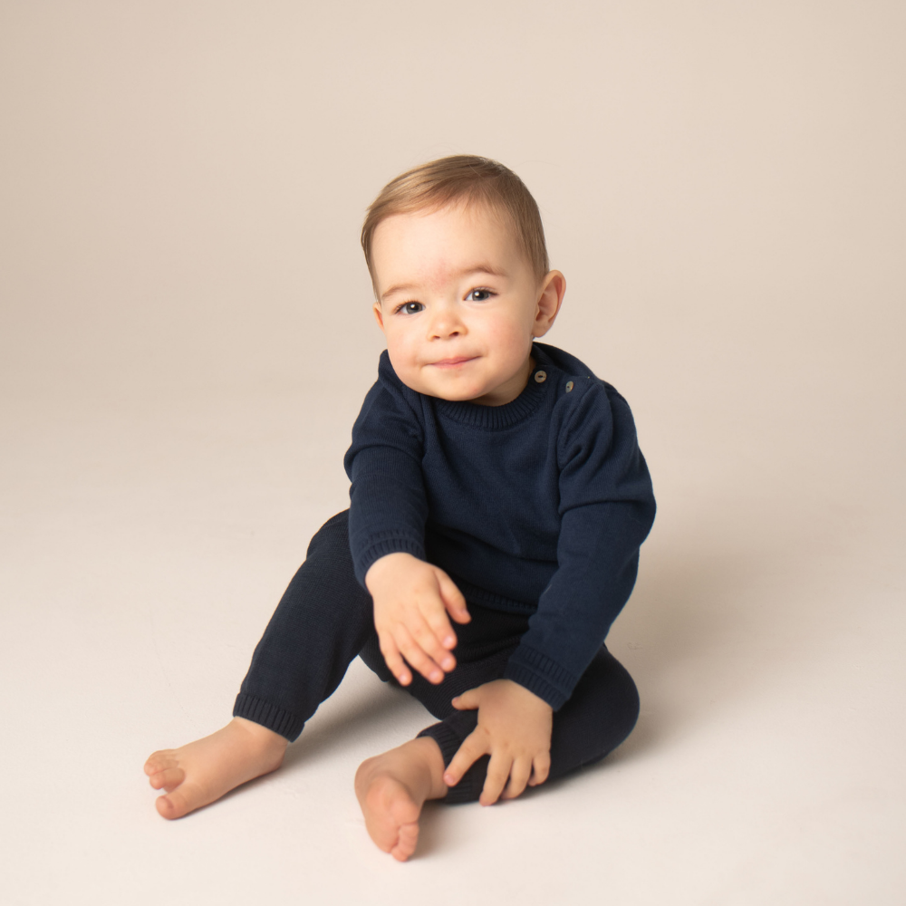 Baby wearing a navy blue outfit sitting on a beige background
