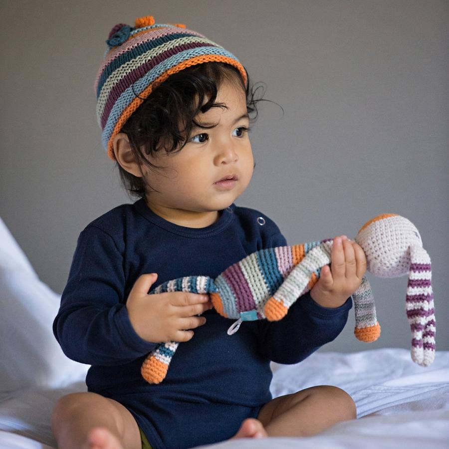 Child wearing a colorful striped hat holding a striped toy on a plain background