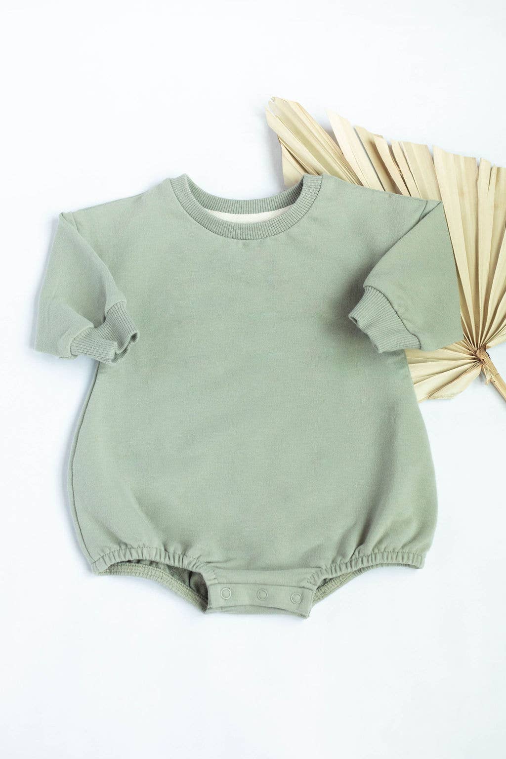 Green baby romper on a white background with dried leaves