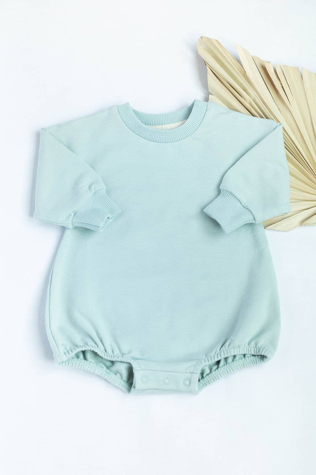 Light blue baby romper on a white background with a beige leaf decoration.