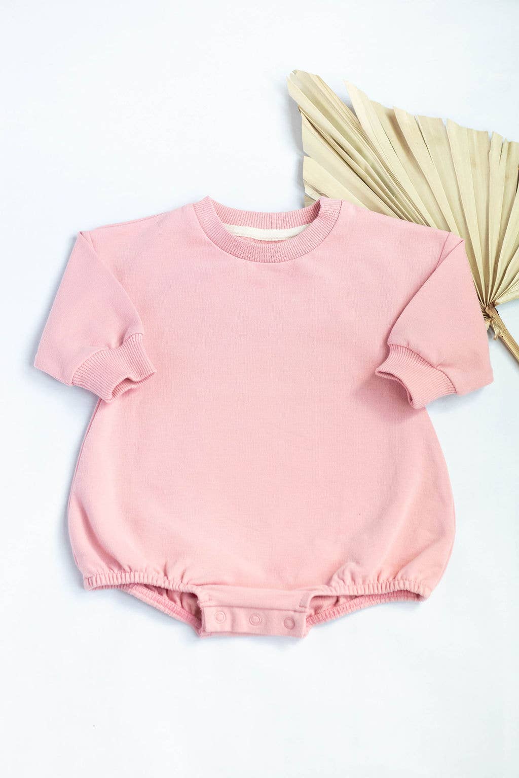 Pink baby romper on a white background with a beige fan