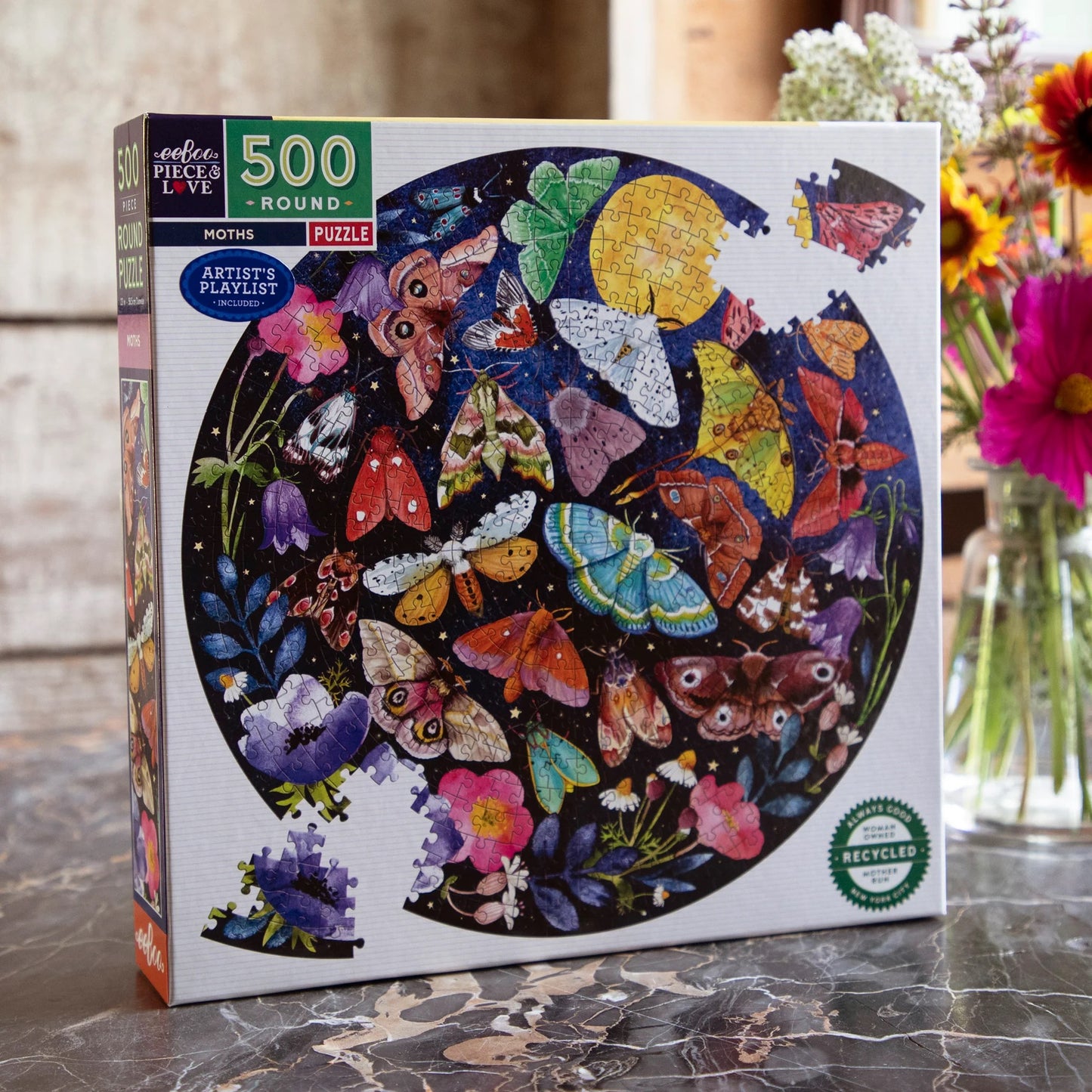 Moths 500-piece Round Puzzle in its box ext to a vase of flowers