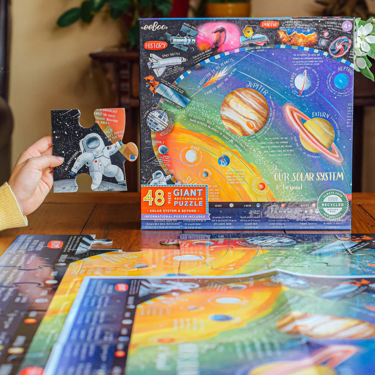 Child holding up a puzzle piece with an astronaut on it next to the box for 48-piece Solar System and Beyond puzzle