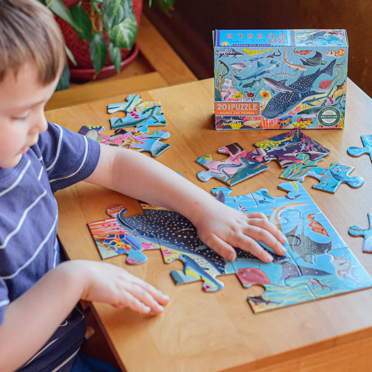 Child wearing a blue shirt with thin white stripes making a 20-piece Sharks & Friends puzzle