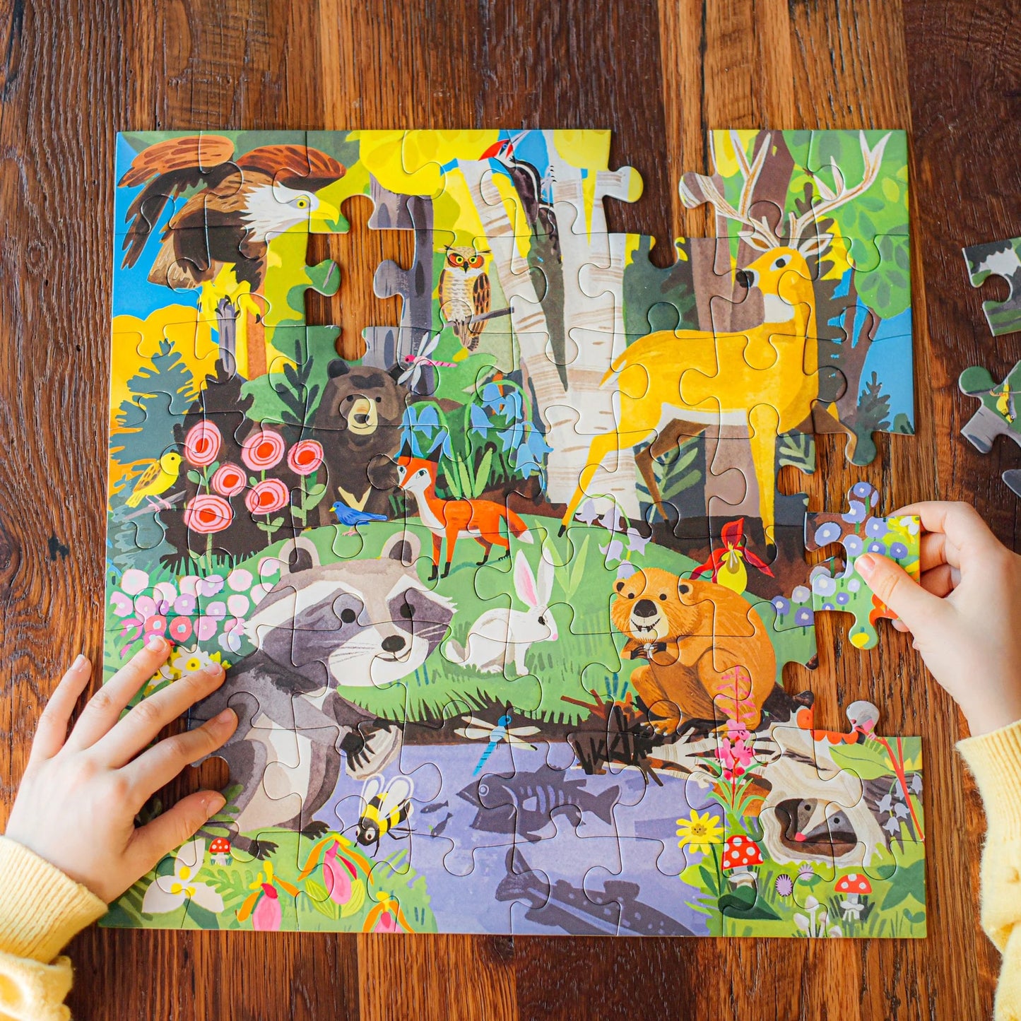 child wearing a yellow sweater making Woodland 64-piece Puzzle on a wooden table