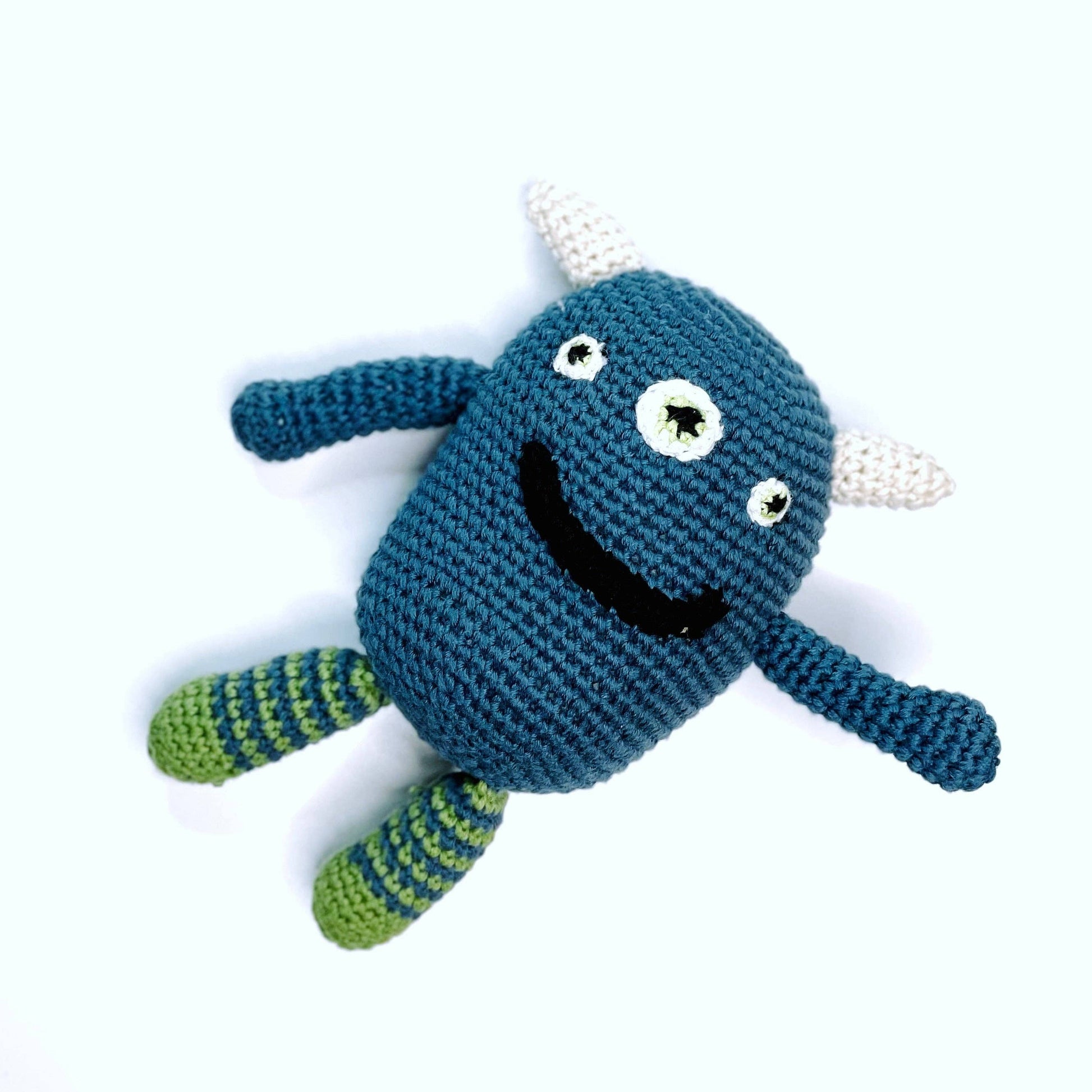 Crocheted blue monster toy with green legs on a white background