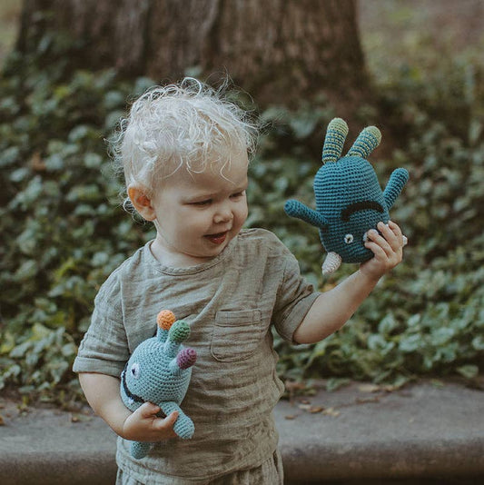 Child holding two blue stuffed animals in front of a natural background