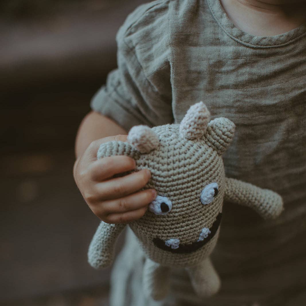Child holding a small crochet dragon toy against a blurred background