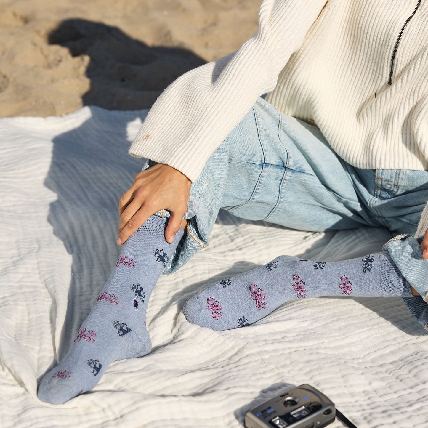 Person wearing light blue socks with floral patterns sitting on a sandy surface.