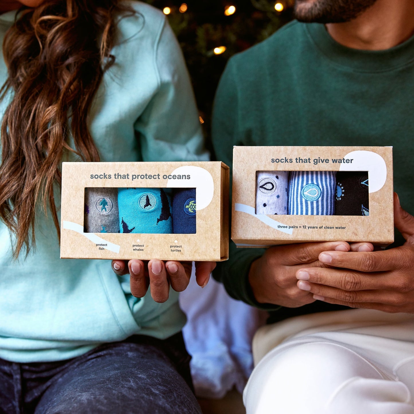 Two people holding boxes of socks with ocean-themed designs.
