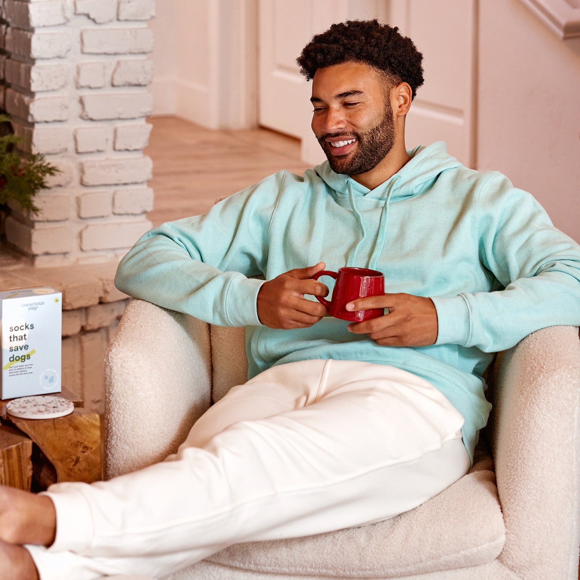 Man sitting on a couch holding a red mug in a cozy living room.