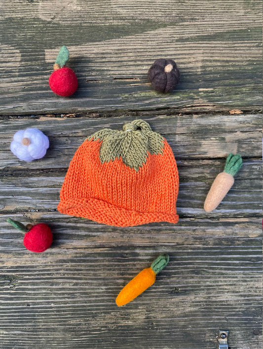 Knitted pumpkin hat with small vegetables on a wooden surface