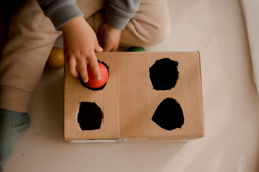 Child playing with a cardboard box resembling a stove with black circles on a beige surface