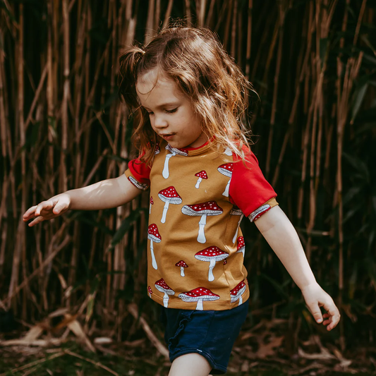 Child walking in front of bamboo wearing shorts and a mushroom raglan by rainbow waters
