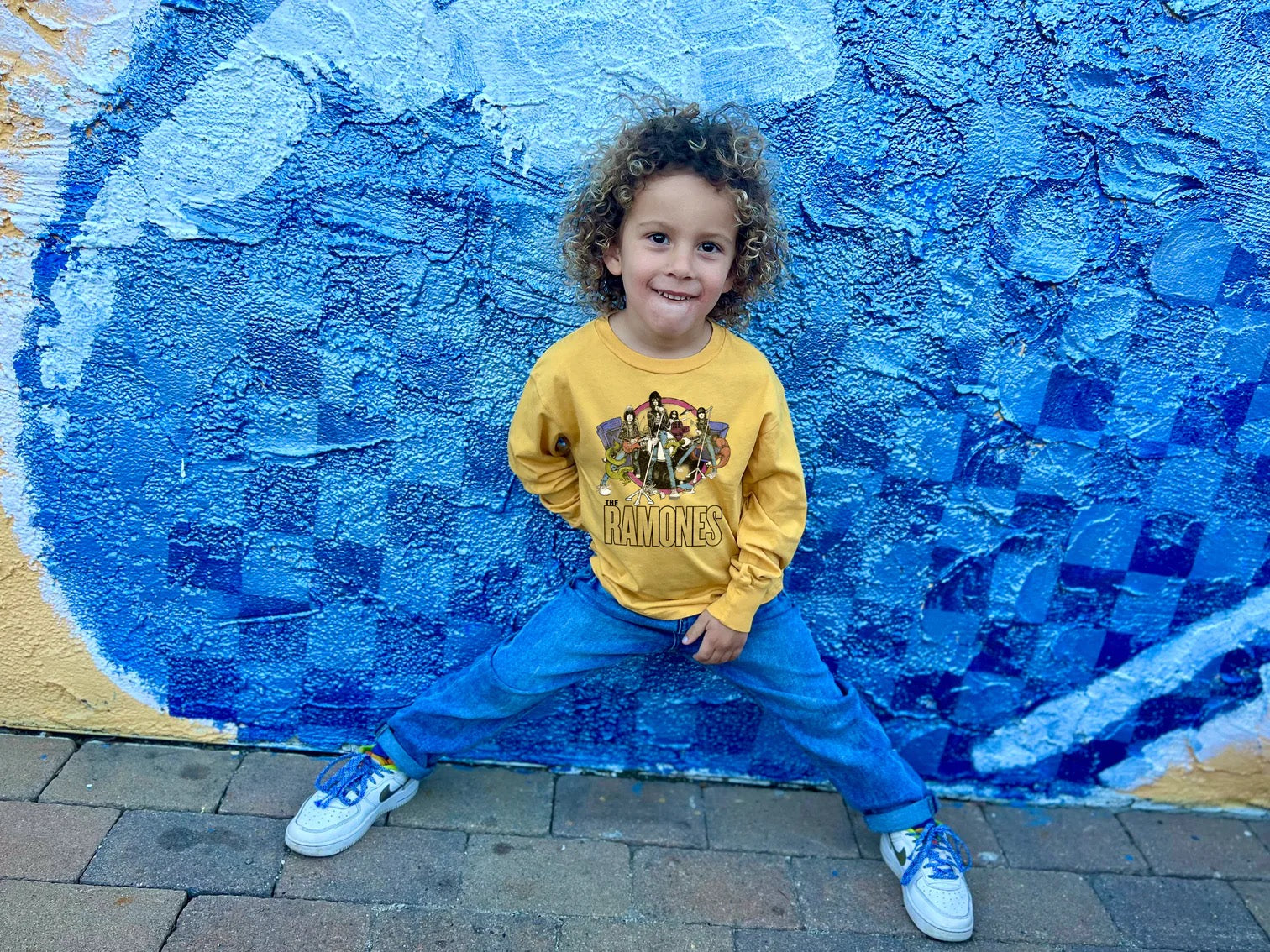 Child standing in front of a blue wall wearing a Ramones long sleeve tee