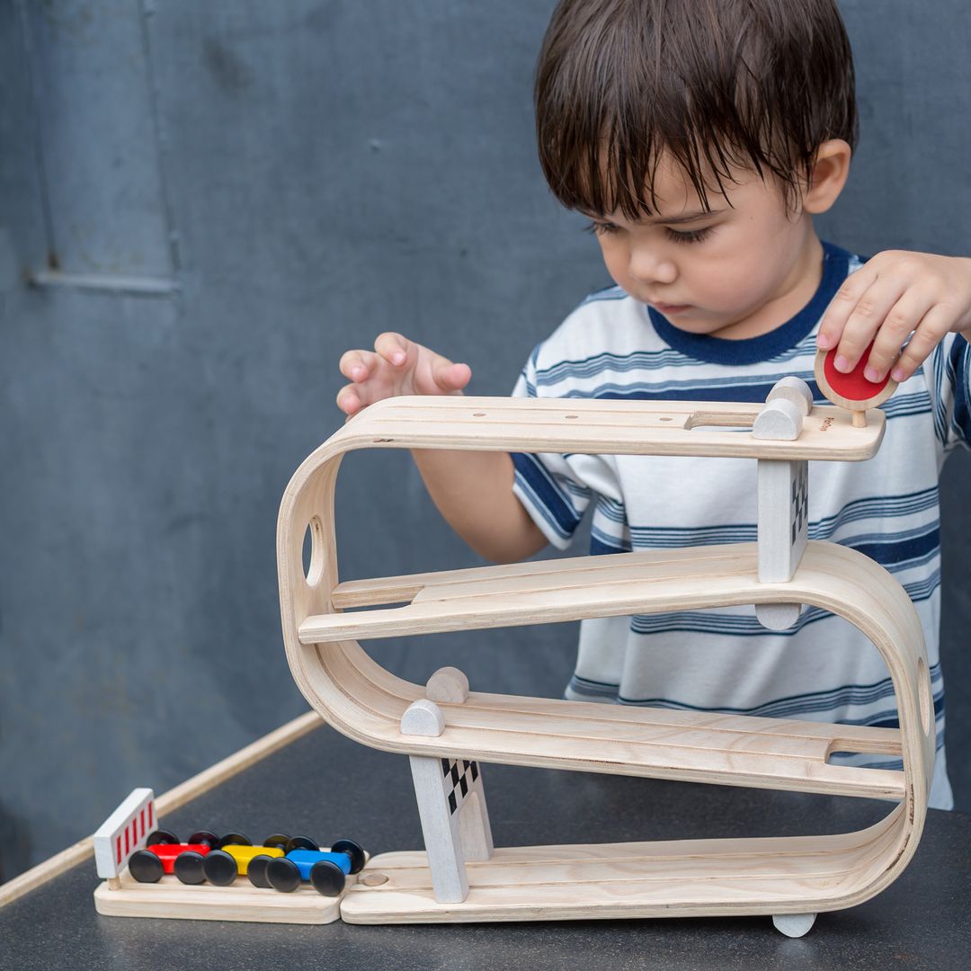 Child playing with a wooden marble run toy against a gray background