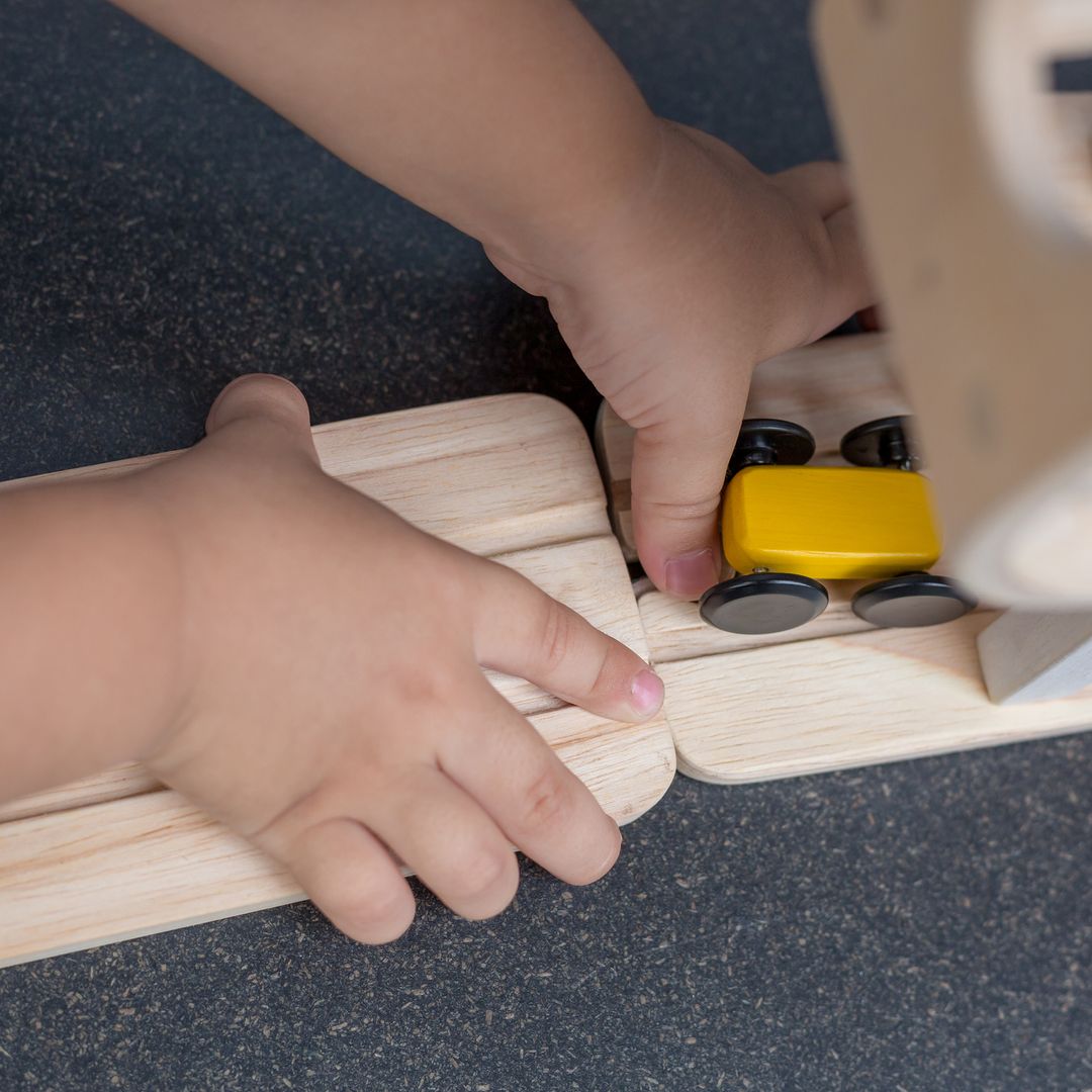 Child's hands playing with a wooden toy train set on a dark surface