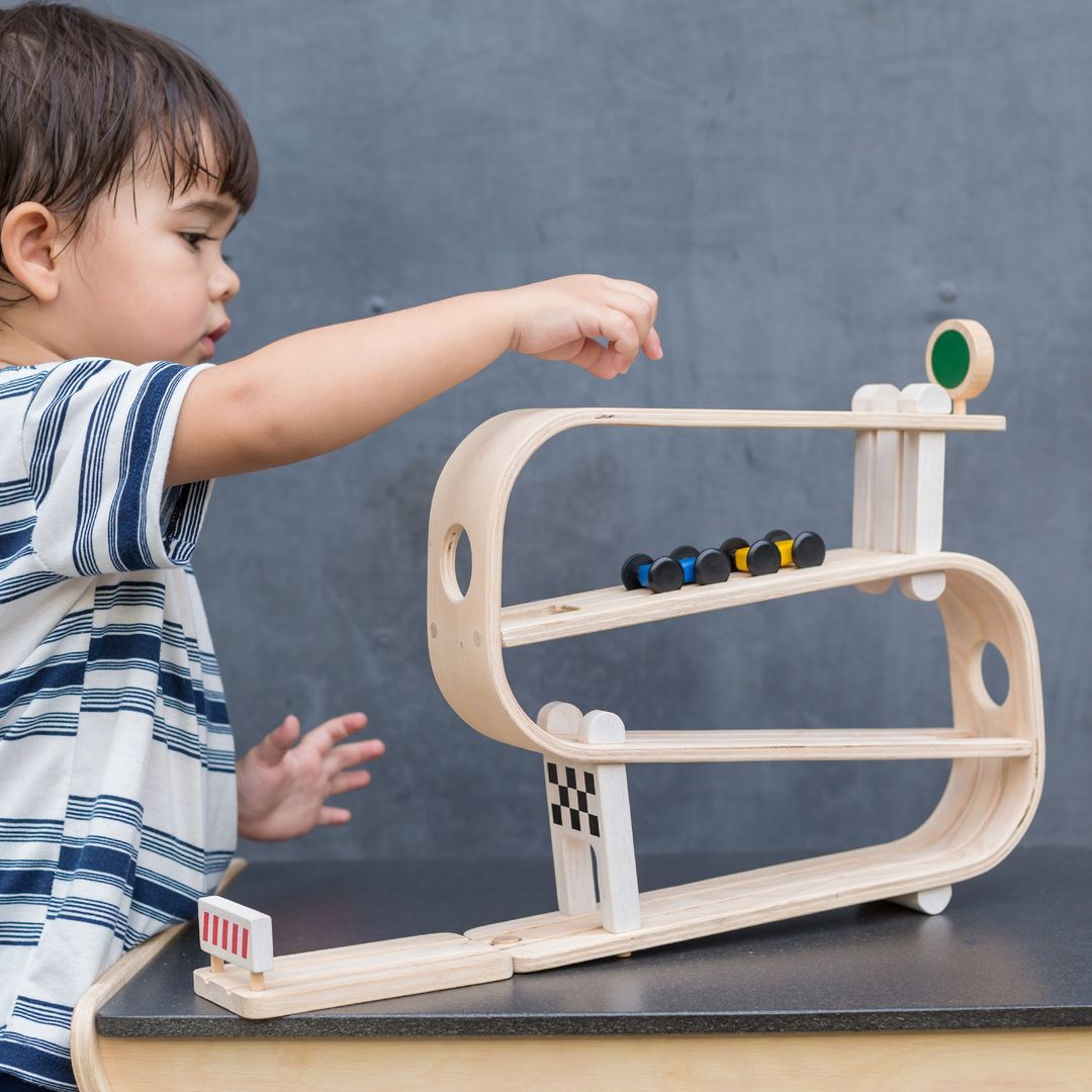 Child playing with a wooden marble run toy against a gray background